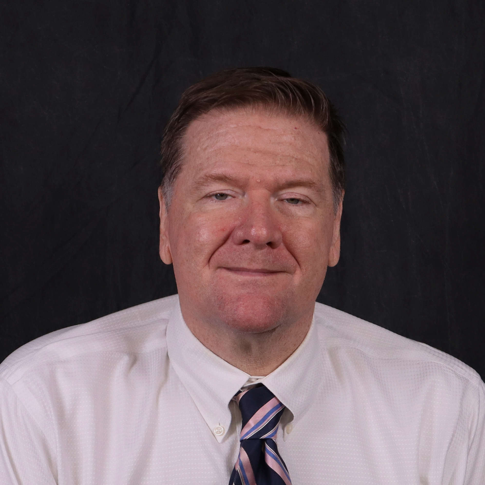 Headshot of Ron Venable with a white shirt and tie against a dark background.